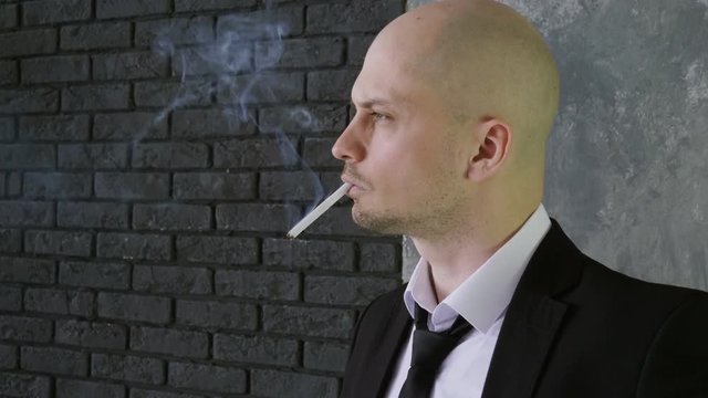 Portrait of handsome man wearing in a black suit, lighting and smoking a cigarette. 4K