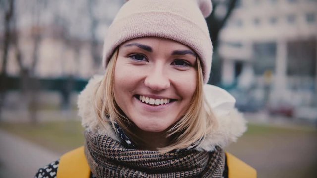 Close-up lifestyle portrait of young beautiful Caucasian girl in winter hat smiling happy, looking at camera on cold day