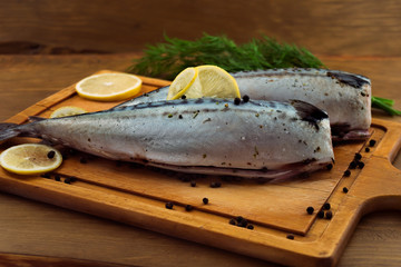 Peeled fresh headless fish with lemon and black pepper on kitchen chopping Board.