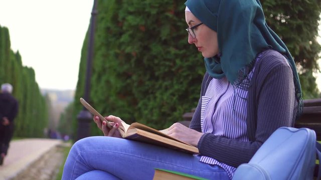 Muslim student i engaged in learning with the help of phone and textbook