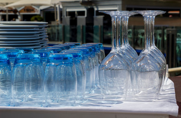 Blue tinted tumblers and wine glasses with plates stacked in a restaurant