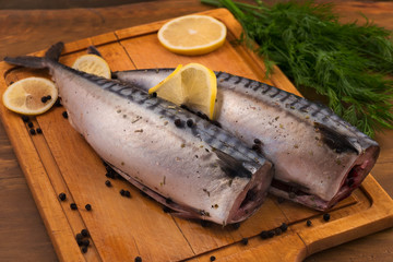 Peeled mackerel in a lemon marinade with black pepper and dill on a chopping kitchen Board.