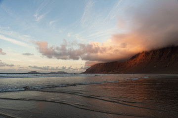 bizarre lines formed by the oncoming waves on a flat shore and a mountain wrapped in clouds at sunset