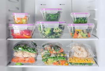 Containers and plastic bags with frozen vegetables in refrigerator