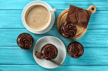 Delicious chocolate cupcakes with cup of coffee on color wooden table