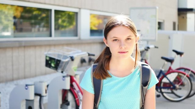 Portrait of inexpressive fifteen-year-old girl by city bikes who then smiles