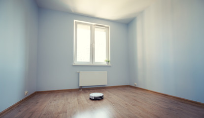 Fototapeta premium White robotic vacuum cleaner on laminate floor cleaning dust in empty room interior