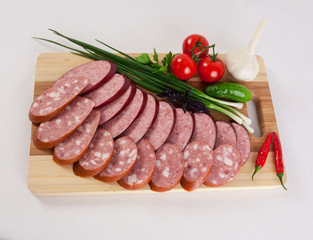 still life with sliced smoked sausage greens and tomatoes on a white background