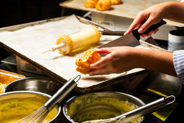 cream cakes in female hands in the kitchen, filling the cakes with cream using a confectionery syringe with women's hands