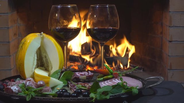 Two glasses of wine, cheese, bread and fruit on fire background, dolly shot