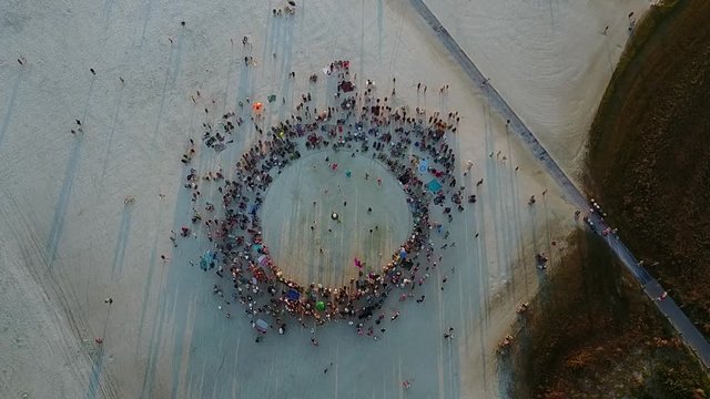 Aerial shot of large drum circle on white sand pointed straight down with a slow push in.