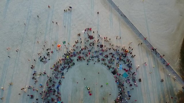Aerial shot pointed down moving quickly over drum circle on white sandy beach at sunset.