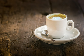 A small espresso coffee cup on a round wooden table outdoors.