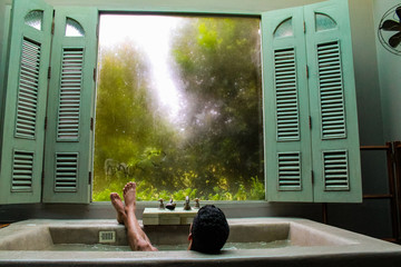 Man relaxing on a luxurious bath tube with a view to a green garden and green windows on a hotel