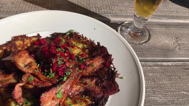 Moving steadyshot of potato pancake with crispy fried pork and lingonberries served outside a lovely summer eavning.