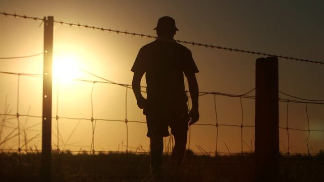 Silhouette of farmer walking away wire fence