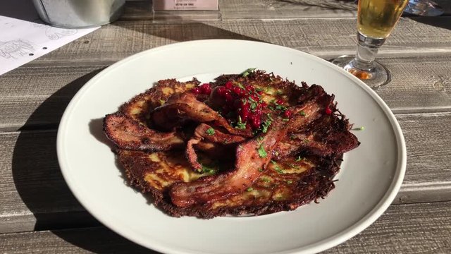Zoom in shot of potato pancake with crispy fried pork and lingonberries served outside a lovely summer eavning.