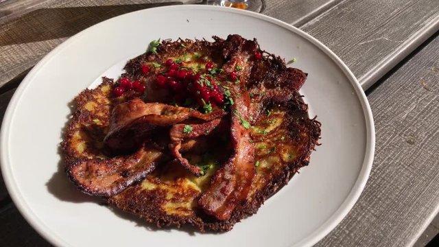Moving steadyshot of potato pancake with crispy fried pork and lingonberries served outside a lovely summer eavning.