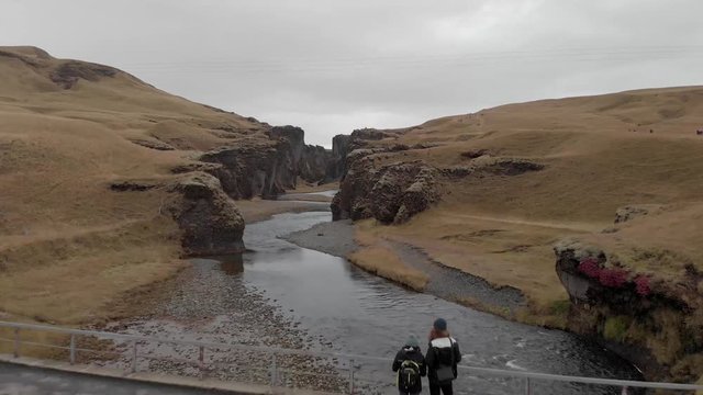 Aerial flyover of a couple stood in front of a stunning Icelandic canyon.