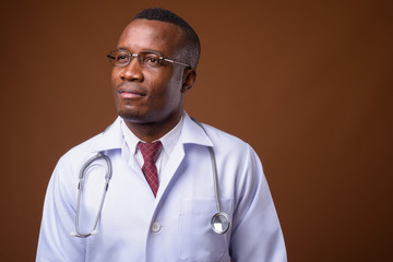 Studio shot of young African man doctor against brown background