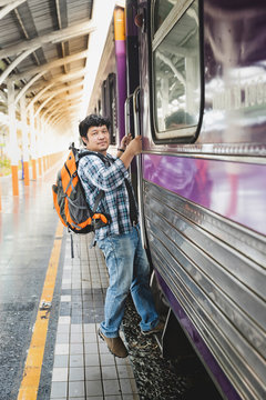 Asian man traveler with backpack is stepping up the train in train station.