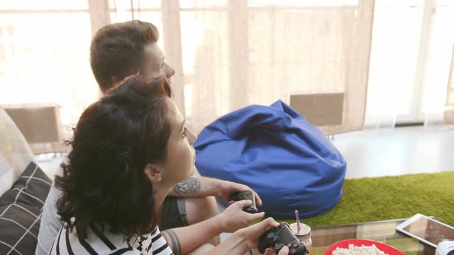 Caucasian couple in love with joysticks in hands playing video game. Good-looking young man and girlfriend spending weekend together. Relationship. Lifestyle. Indoors.