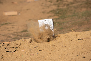 Target practice aim at the outdoor range. Bullet hits the ground sending dust and particles up into...