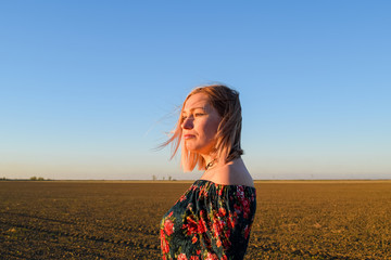 Obraz premium Woman in a plowed field in a red-black dress on a sunset background
