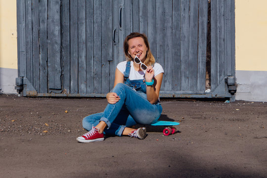 Portrait of a smiling woman sitting on her skateboard next to the old wooden wall.