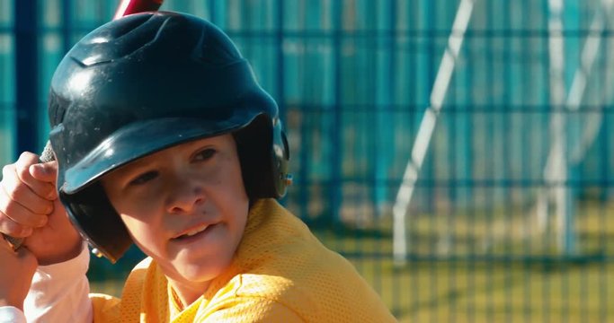 CU Portrait of kid boy batter baseball player hits a ball during a game. 4K UHD 60 FPS SLO MO RAW