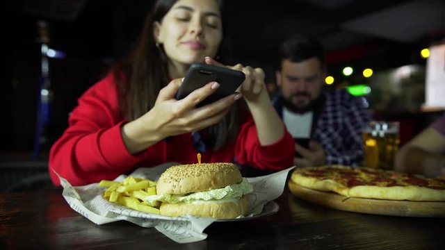 A girl in the company of a man taking pictures on your smartphone your Burger at the bar.