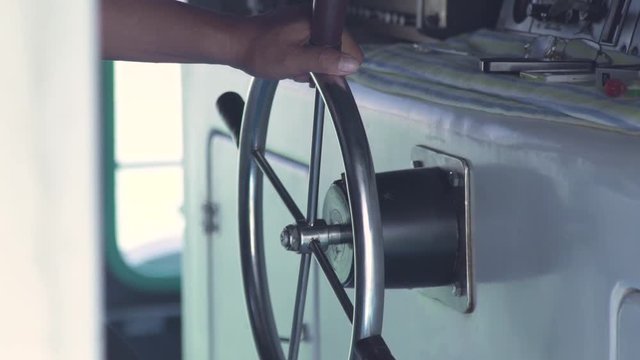 Close up male hand of captain on steering wheel of sailing ship in captain bridge on blue sea landscape. Ship wheeel of sailing boat in sea.