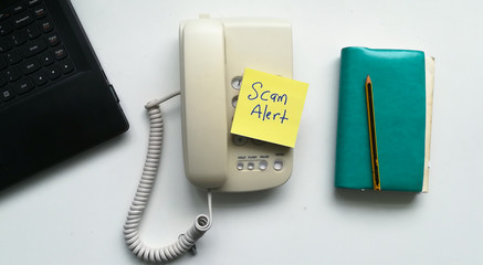 Yellow sticky note with text scam alert on a telephone.
