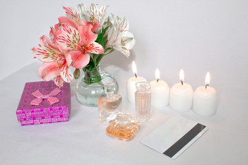 Picture of a pink luxury gift box with a bouquet of beautiful Alstroemeria flowers, a romantic candle, perfume and a credit card. Dressing table with women's accessories.