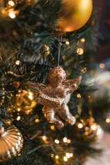 Cute toy golden angel hanging on decorated Christmas tree with gifts in cozy home