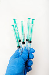 hand in blue glove holding many empty syringes on white background