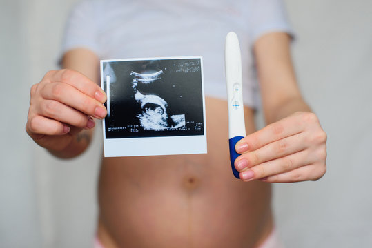 ultrasound picture and positive pregnancy test in the hands of a pregnant girl on the background of the abdomen