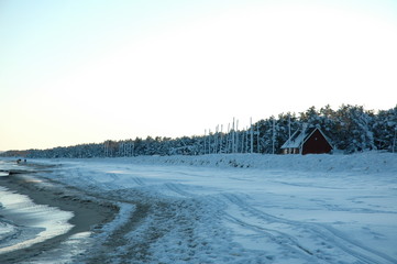 Landscape with snowy beach, red house and trees with people walking
