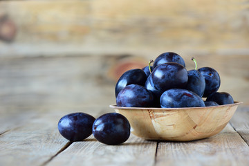 Fresh plums in bowl on wooden background