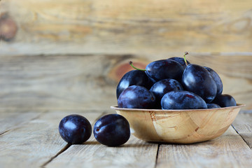 Ripe blue plums in a wooden bowl on a wooden background