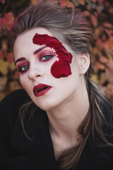 Beautiful young girl with applique red roses flowers on the face in nature autumn