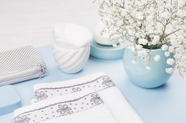 Fashion cosmetic products - white soap, towel, flowers, soap dispenser, blue ceramic vase, silver cosmetic bag on white wood background, closeup.