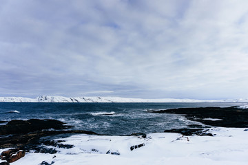 Fototapeta na wymiar rocky coast of blue cold ocean in the north covered with snow in a winter frosty day