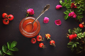 Spoon in a jar of rosehip jam and its berries with leaves nearby, top view - 228456125
