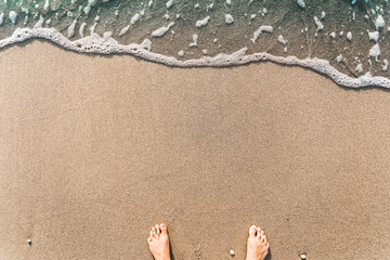 Sandy beach with waves on it and with male feet. Background with place for text.