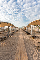 Rows of sun loungers on a sandy beach with sun shades. Relaxation and luxury beach holidays