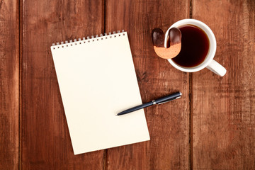 A photo of a blank page of a spiral notebook, with a cup of coffee with a cookie, shot from the top on a dark rustic wooden desk with a place for text