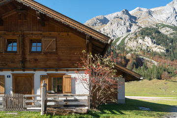 Traditional wooden alpine houses decorated with flowers on green meadow in Grosser Ahornboden am Karwendel mountain village on sunny summer day, Tyrol, Austria