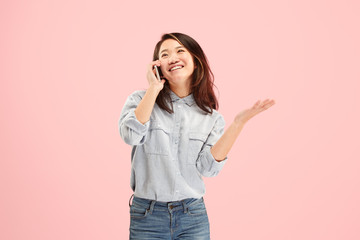 Young beautiful woman using mobile phone studio on pink color studio background. Human facial emotions concept. Trendy colors