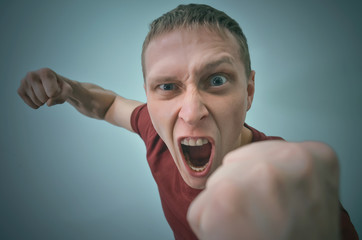 Angry man in stress is shouting and is shaking by his fist isolated on blue background.